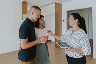 Smiling agent giving house key to couple standing at home