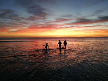 Silhouette people on beach against sky during sunset