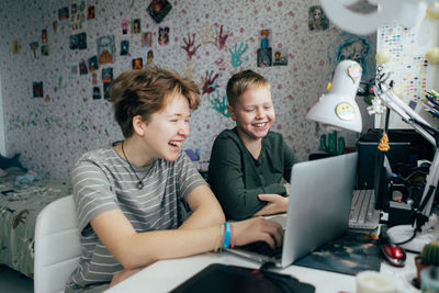 Laughing cheerful brother and sister are watching entertainment video content on a laptop.