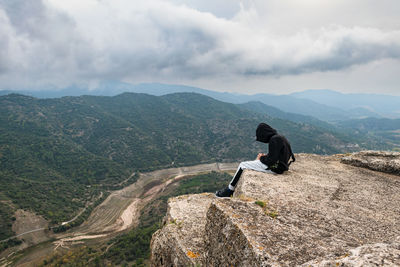 Teenager sit down sat on the edge of a cliff while storm is coming
