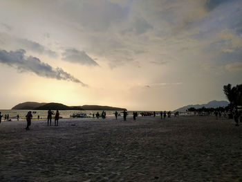 Group of people on beach against sky during sunset
