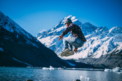 Man jumping in mid-air by snowcapped mountains against sky