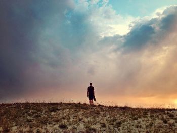 Silhouette of woman standing on field against cloudy sky