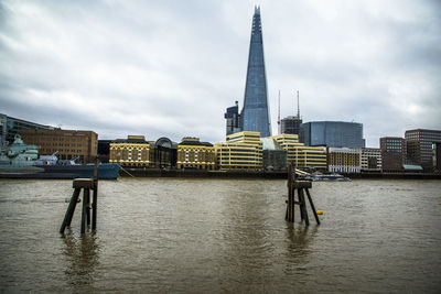 View of buildings by river against cloudy sky