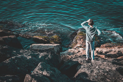 Young man standing on rock by sea