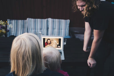 Man looking at mother and daughter doing video conference on laptop in holiday villa