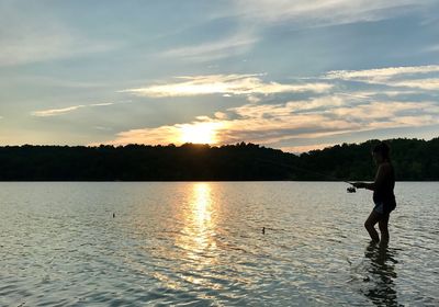 Man fishing in lake against sky during sunset