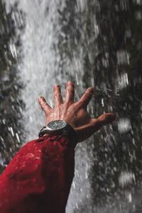 Cropped hand of person gesturing against waterfall
