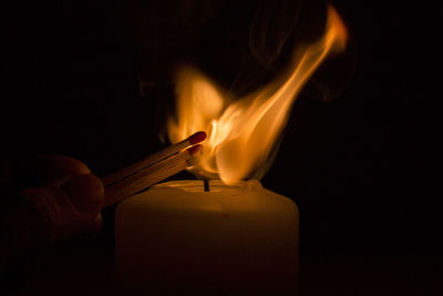 Cropped image of person igniting candle in darkroom