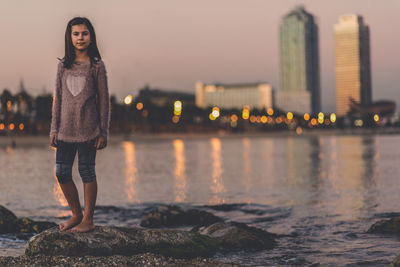 Portrait of young woman standing on rock by water