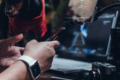 Midsection of man using mobile phone with dog against computer screens in the room at night