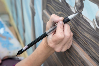 The hand of a woman artist paints the detail of the mural with a brush