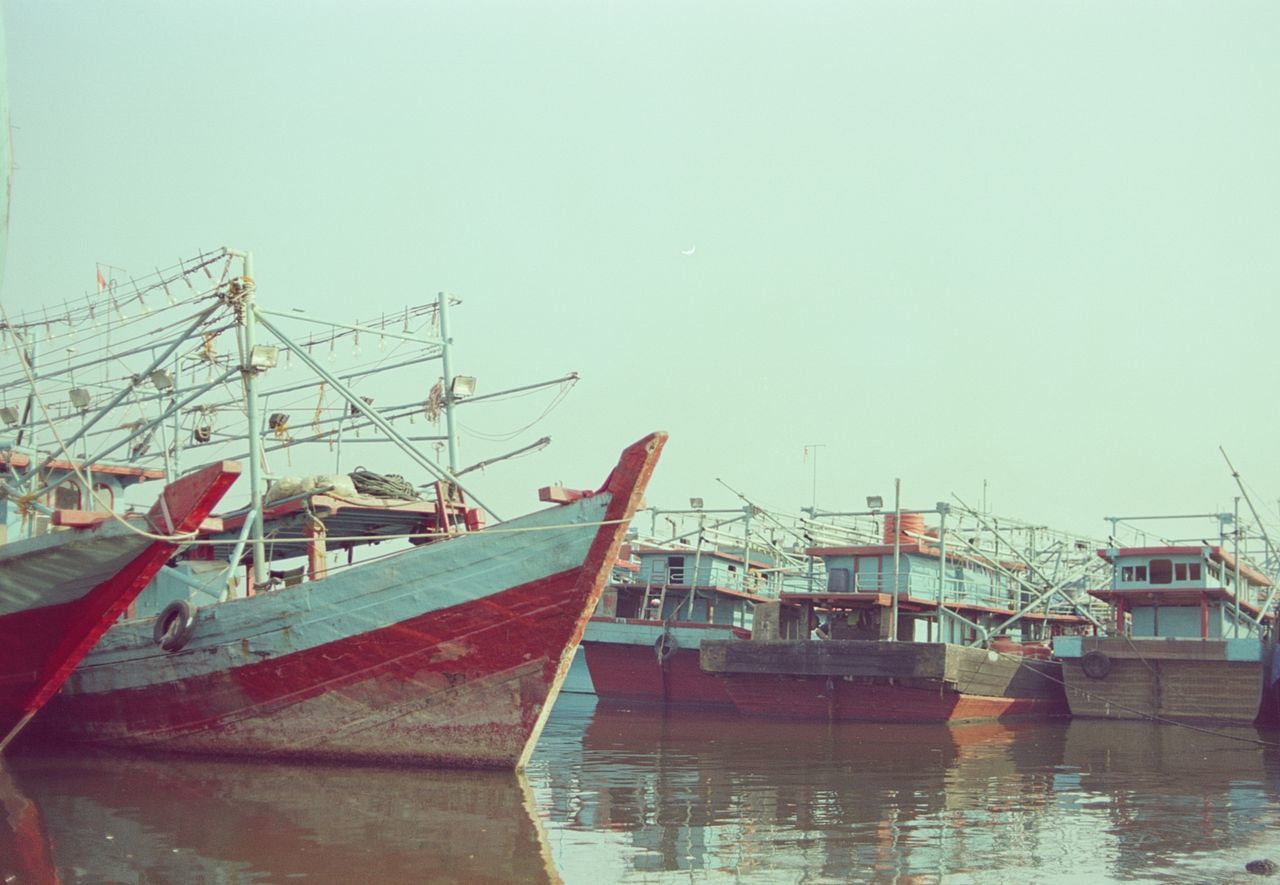 SAILBOATS MOORED IN HARBOR AGAINST CLEAR SKY