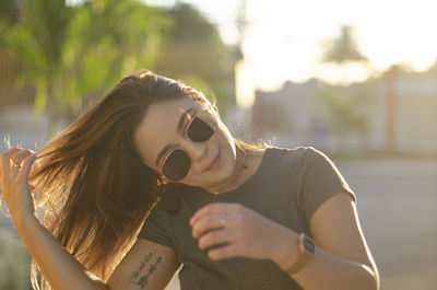 Young woman wearing sunglasses tossing hair while standing outdoors