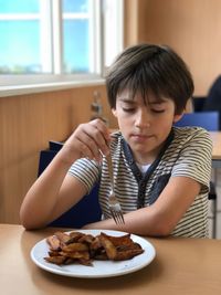 Boy having potato chips while sitting on chair at restaurant