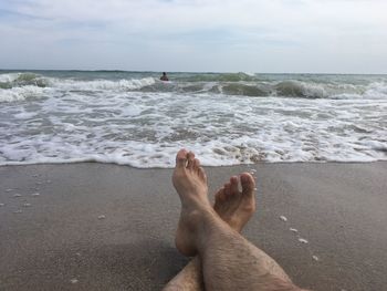 Low section of person on beach against sky