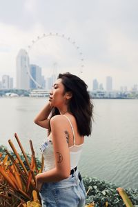 Fashionable young woman standing against sea and urban skyline