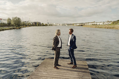 Two businessmen standing on jetty at a lake talking