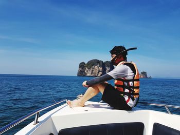 Man sitting on boat over sea against sky