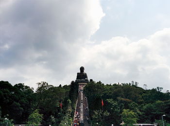 Low angle view of tian tan buddha against cloudy sky