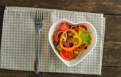 Vegetable salad in a heart shape plate on a wooden table on a napkin. horizontal photo