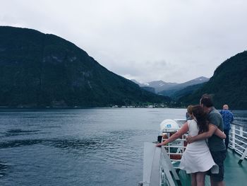 Rear view of people on boat in sea against mountains and sky