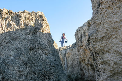 Low angle view of woman standing on rock against sky