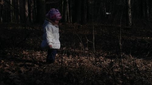 Girl standing on field by trees in forest