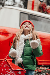 Cute smiling girl standing against car during winter