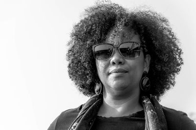 Portrait of woman with curly hair wearing sunglasses against white background