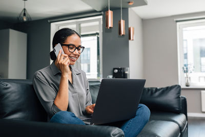 Smiling woman talking over mobile phone while sitting on sofa at home