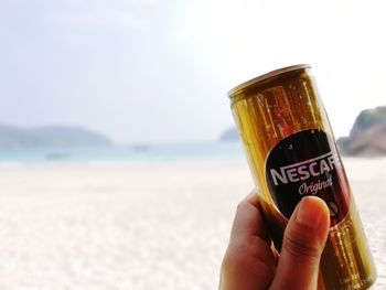 Close-up of hand holding drink at beach against sky