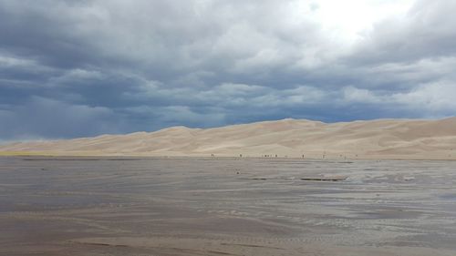 Scenic view of sand dunes against cloudy sky