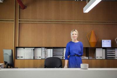 Portrait of smiling businesswoman standing at desk in office