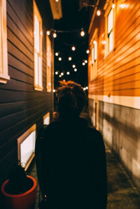 Rear view of woman standing on alley amidst buildings at night