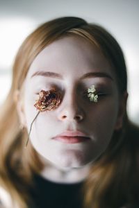 Close-up portrait of young woman with flowers on eyes