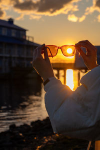 Optical illusion of woman drinking water against sky during sunset