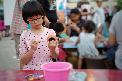 Girl painting earthen pot at table outdoors