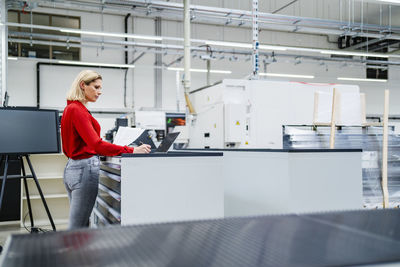 Businesswoman working on laptop standing by table in factory