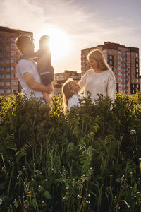 People standing by plants against sky during sunset