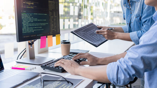 Midsection of computer programmers using computer on office desk