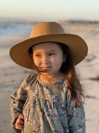 Cute girl wearing hat looking away standing on beach
