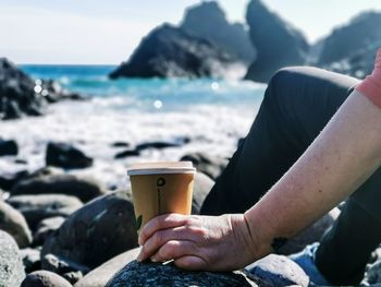 Midsection of man holding rock at beach against sky