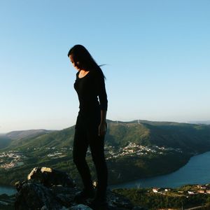 Woman standing on mountain against clear blue sky