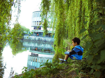 Rear view of woman sitting by plants against trees