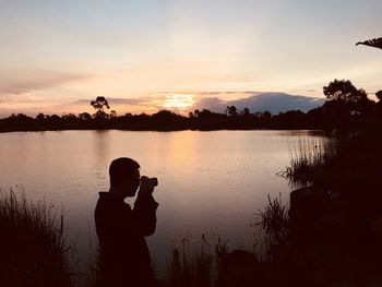 Man photographing lake against sky during sunset