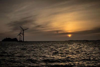 Silhouette of traditional windmill by sea against sky during sunset