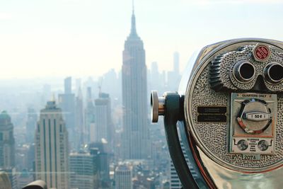 Close-up of coin-operated binoculars and cityscape against sky