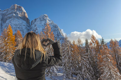 Blonde girl seen from behind drawing a heart with her hands