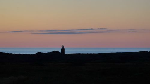 Silhouette lighthouse by sea against sky during sunset